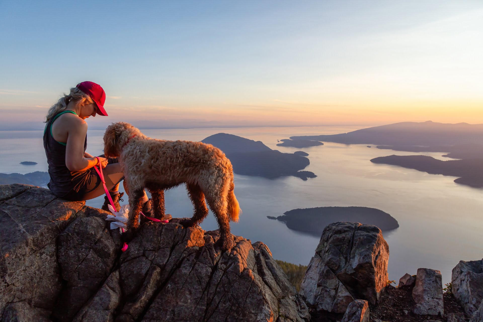 A woman sitting on a mountain peak with her dog