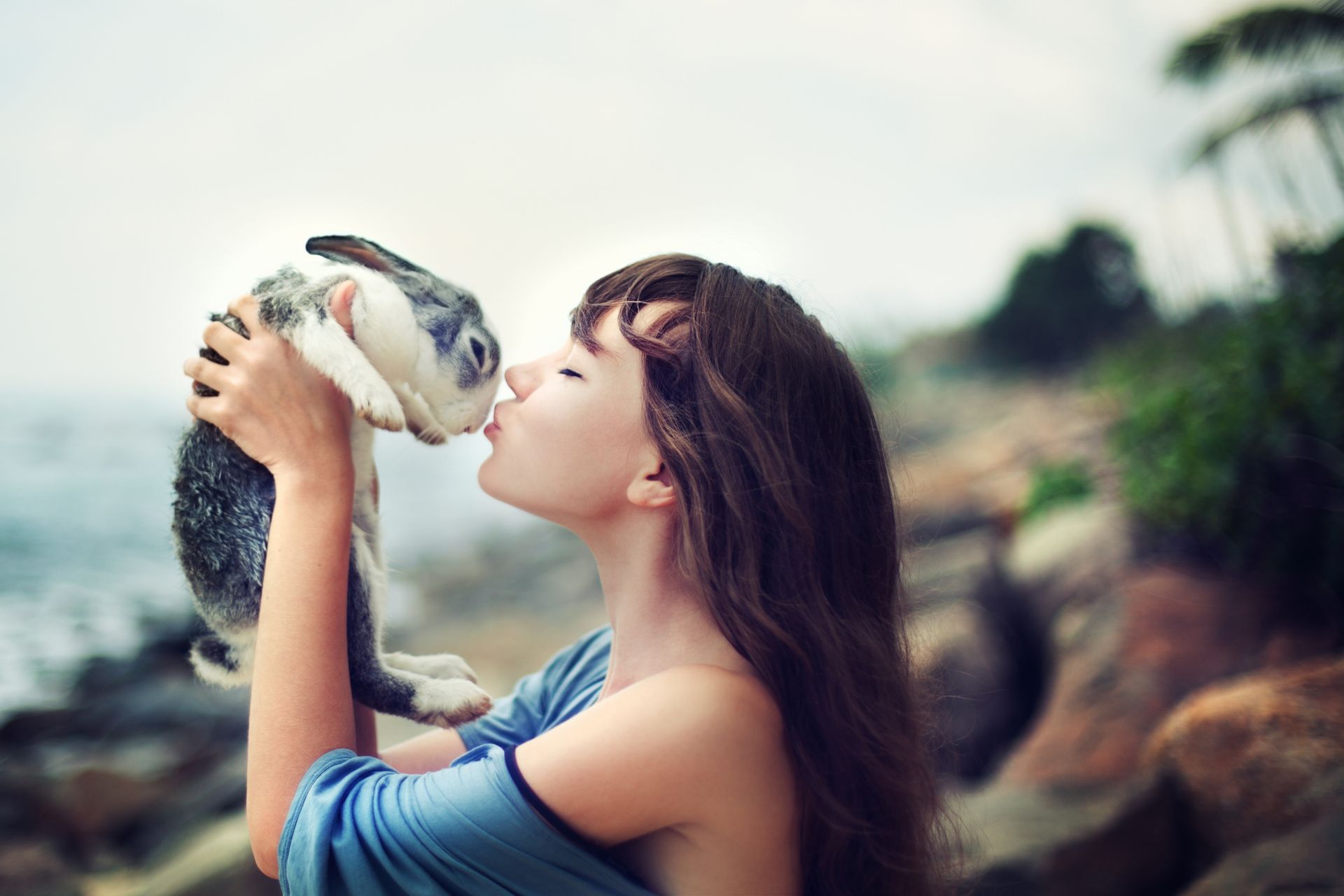 A woman holding a pet rabbit in the air and kissing it