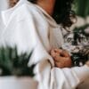 Persona che tiene un gatto grigio in un ambiente interno con piante.