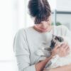 A woman in a light sweater lovingly holds a fluffy cat with blue eyes in a bright, modern room, showcasing the bond between pet and caregiver.