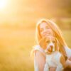 A woman holding a beagle in a sunny field at sunset.