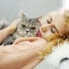 A woman cuddling a gray cat while lying on a couch.