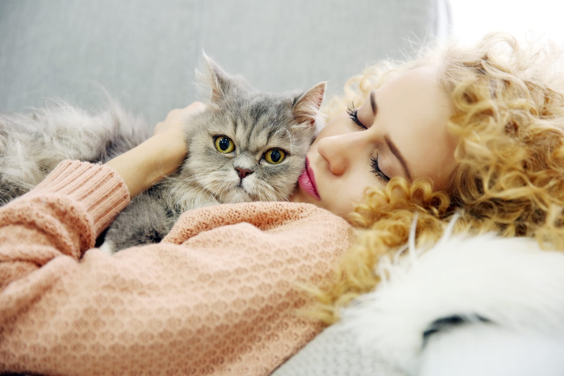 A woman cuddling a gray cat while lying on a couch.