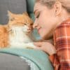 A woman with an orange cat on a couch, touching noses.